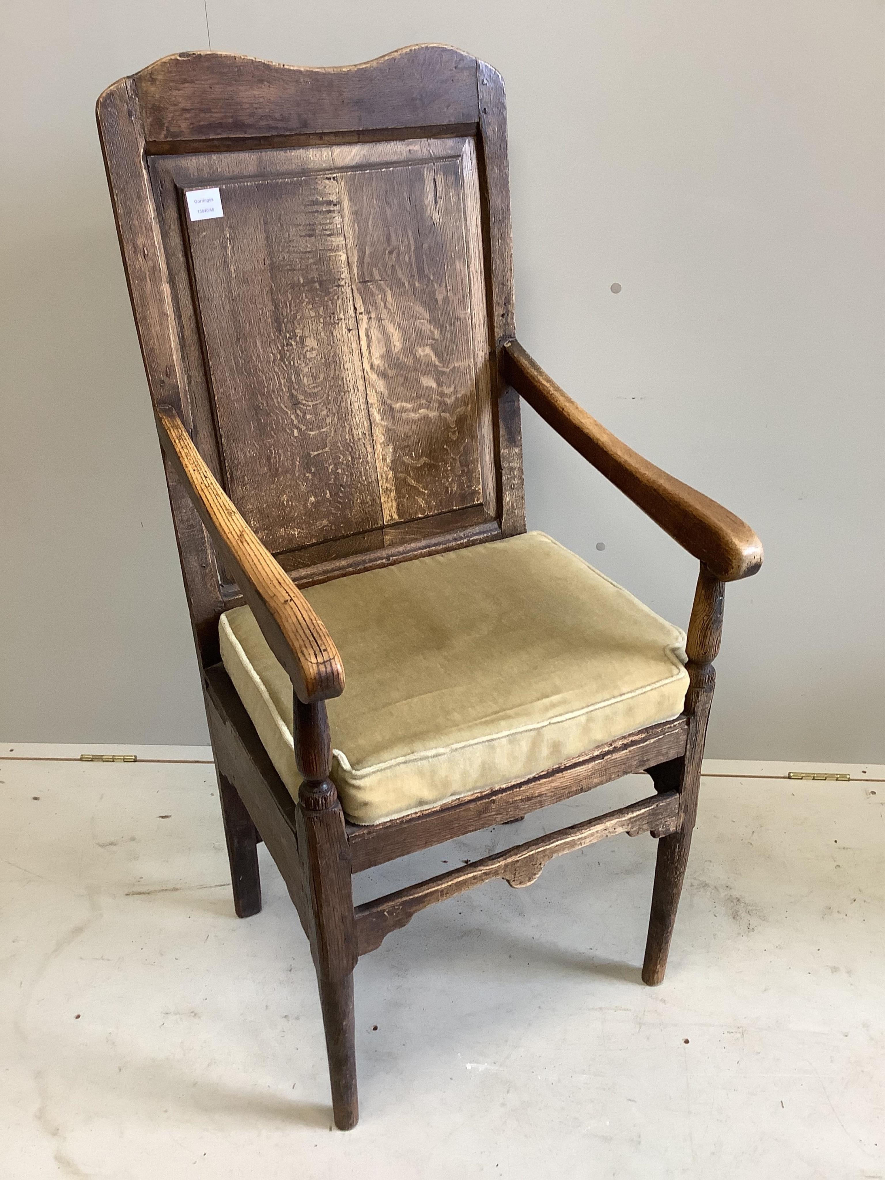 An early 18th century oak panel back open armchair, width 56cm, height 123cm. Condition - faded and worn with a missing drawer beneath the seat